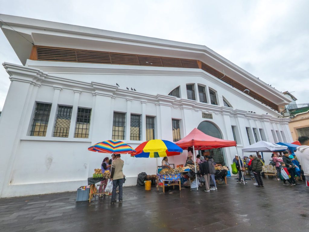 Customers shop from street vendors with colorful umbrellas outside of 9 de Octubre Market in Cuenca, a popular local shopping spot.