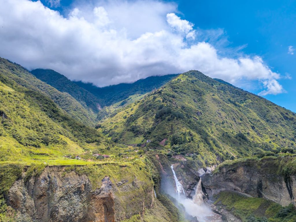 A panoramic view of the green Andes mountains surrounding a powerful waterfall plunging into a rocky canyon along the Ruta de las Cascadas in Baños, Ecuador.