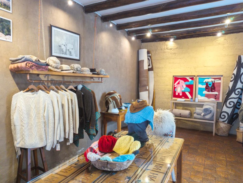 Interior of the cozy artisan shop All Things Alpaca, one of the best shops in Cuenca, Ecuador. On display are handwoven sweaters hanging on wooden hangers as well as hats and scarves.