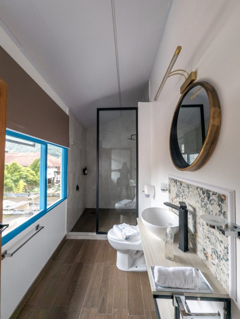Modern hotel bathroom with a vessel sink, round brass mirror, and a walk-in glass shower, overlooking the scenic views from Hotel Mi Pueblo, one of the best places to stay in Baños, Ecuador.