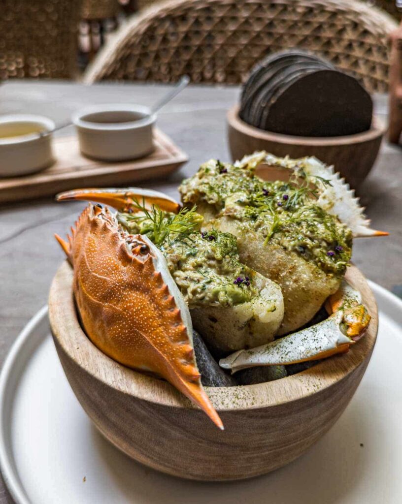 At a restaurant for some of the best seafood in Mexico City, a crab shell sits in a small bowl with crab claws on the side. Inside the bowl is the dish - a crab salad stuffed into arepas. On the table in the background is a bowl of blue corn tostadas and small bowls of salsa.