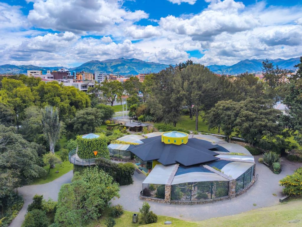 Aerial view of the bird sanctuary at the Pumapungo Museum in Cuenca Ecuador surrounded by trees and cityscape, with the Andes mountains in the distance.