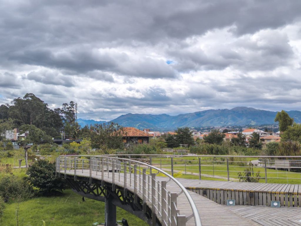 Curved wooden walkway at the Botanical Gardens in Cuenca Ecuador with lush greenery and views of the Andes mountains under a cloudy sky.