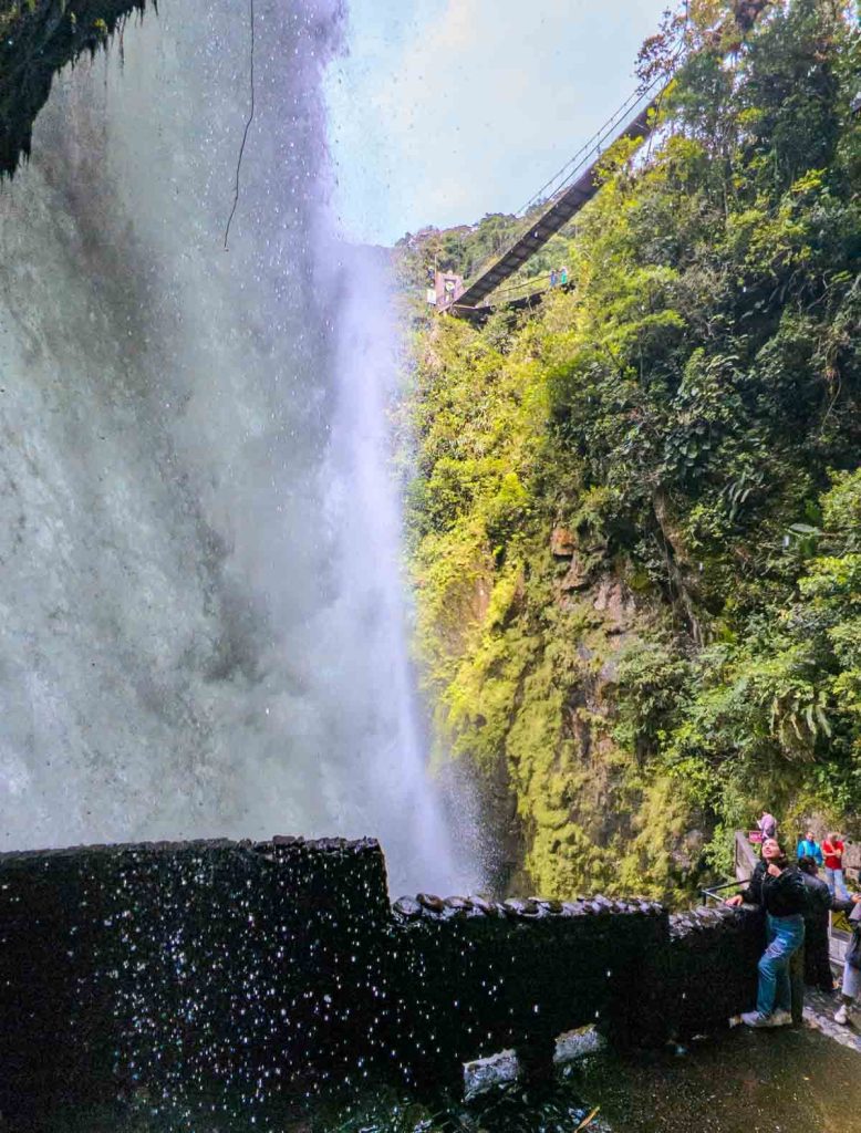 Close-up of powerful water spray from Cascada Pailón del Diablo as visitors stand on a viewpoint, surrounded by mossy cliffs and jungle.
