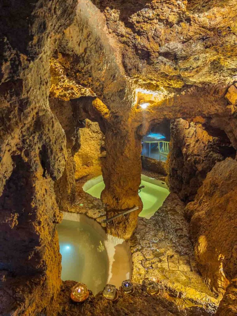 Underground thermal baths at Piedra de Agua in Cuenca Ecuador, with candlelit rock walls and two mineral-rich hot spring pools (one hot and one cold) glowing in the warm cave light
