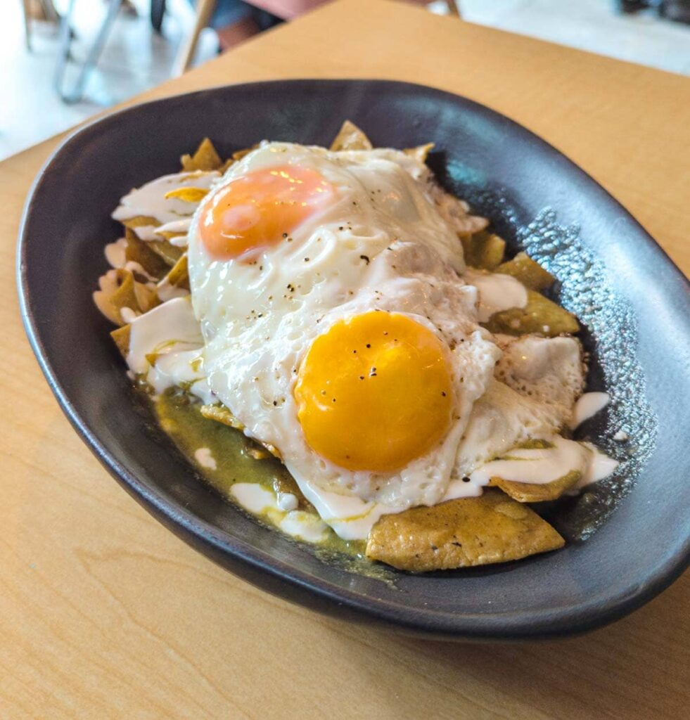 A plate of chilaquiles in Mexico City is served in a black bowl with two sunny side up eggs on top.