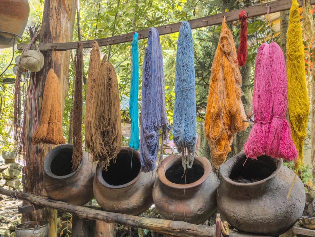 Colorful skeins of natural-dyed yarn hanging above clay pots in a traditional workshop of weavers in Gualaceo, one of the artisan day trips from Cuenca.