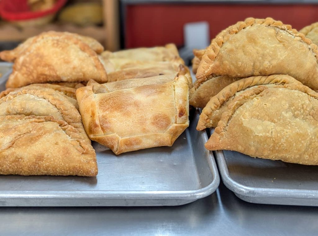 A tray of freshly baked and fried empanadas de verde made with green plantain dough, some folded into half-moons and others shaped into neat rectangles. These savory pastries are a traditional Ecuadorian food from the coast, often filled with cheese or meat and enjoyed as a snack or breakfast.