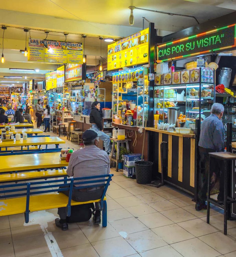 Dining area inside Mercado 10 de Agosto Cuenca, with yellow tables and traditional Ecuadorian food stalls serving locals and tourists alike.