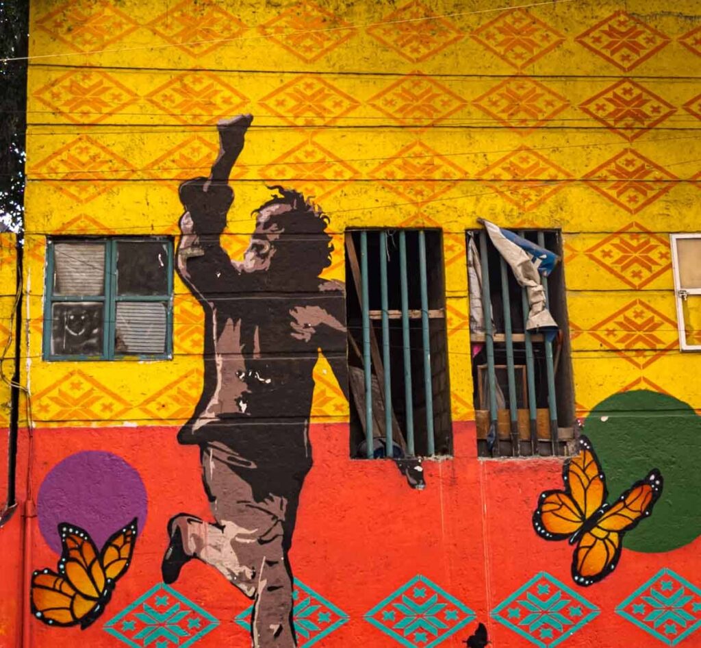 This street art in Centro Mexico City depicts Francisco Toledo flying a kite with two butterflies on a yellow background.