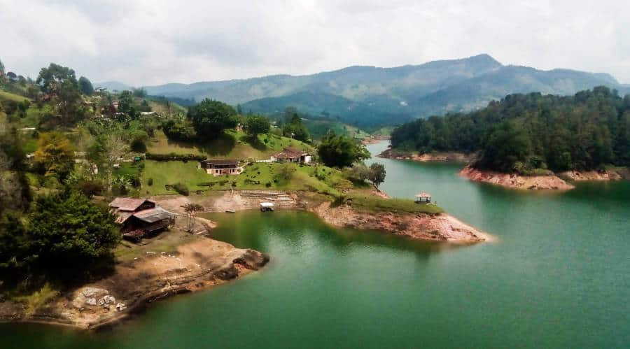 Sandy islets jut out into blueish green water of Guatape lake with a mountain ridge in the background.