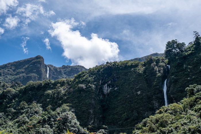 Two narrow waterfalls cascade down lush mountain cliffs under a bright blue sky in Giron, an adventurous day trip from Cuenca.