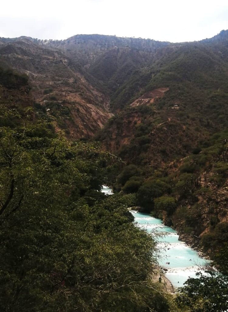 A bright blue thermal pool runs through the property at Tolantongo, Hidalgo surrounded by green mountains.