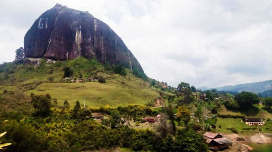 The Guatape rock juts out of the green hillside with a few cabins below.