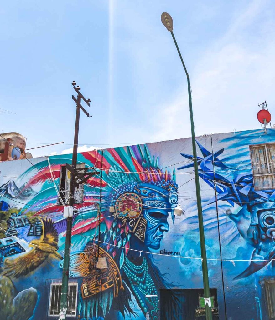 This Mexico City street art in predominantly blue colors depicts an Aztec warrior wearing a headdress and jewelry.