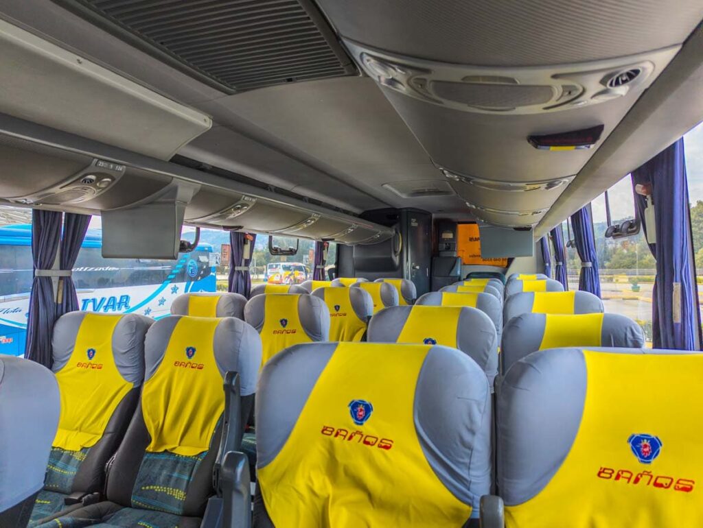 Plush seats on the Quito to Baños bus with luggage storage above and yellow seat covers stitched with red lettering that says Baños.