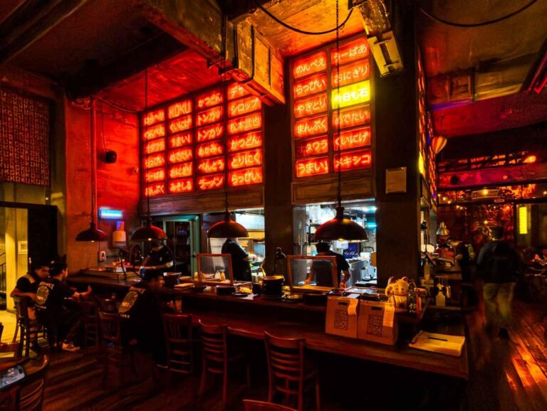 At Koku, a Japanese restaurant in Mexico City, lights above the bar shine red with Japanese lettering. Behind the bar are two views into the kitchen.