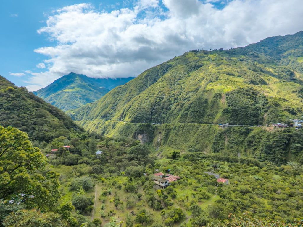 A sweeping view of a green valley dotted with small houses, with steep mountain ridges framing the background along the Ruta de las Cascadas near Baños.