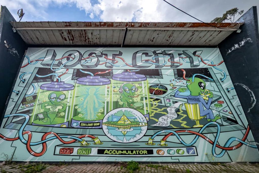 A vibrant mural labeled “Lost City” features aliens, laboratory tanks, and sci-fi graphics, located near the base station of the cable car in Quito Ecuador.