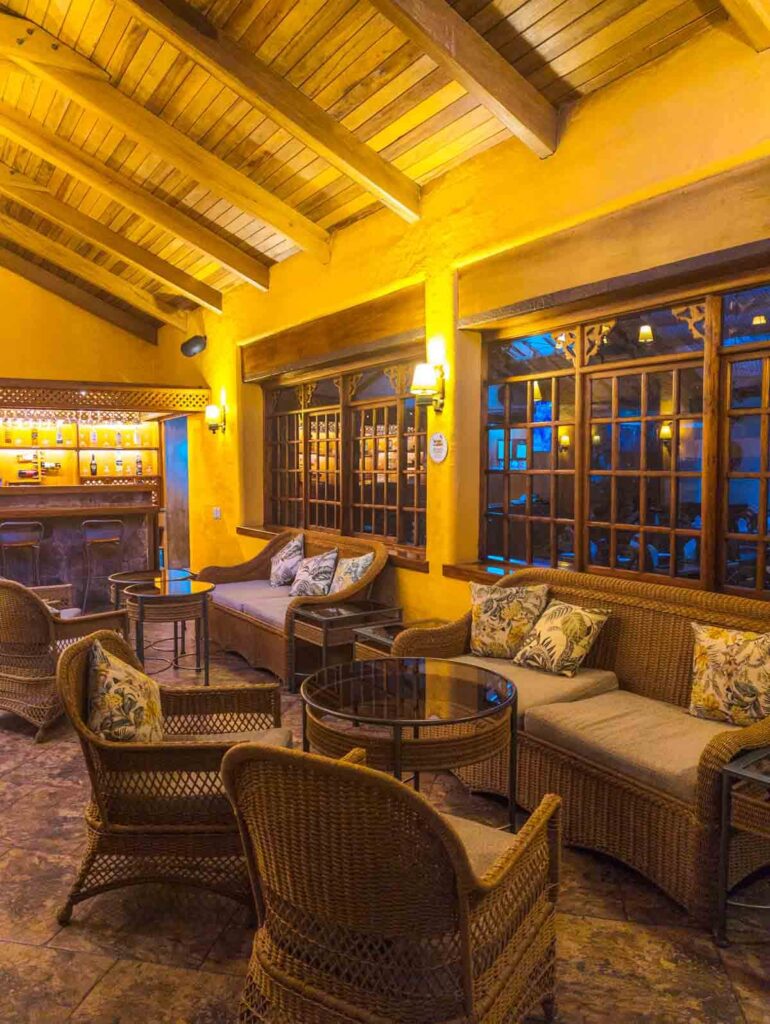 The lounge at the Papallacta hot springs resort features tall wood beam ceilings with couches, chairs, and tables in front of the bar area.