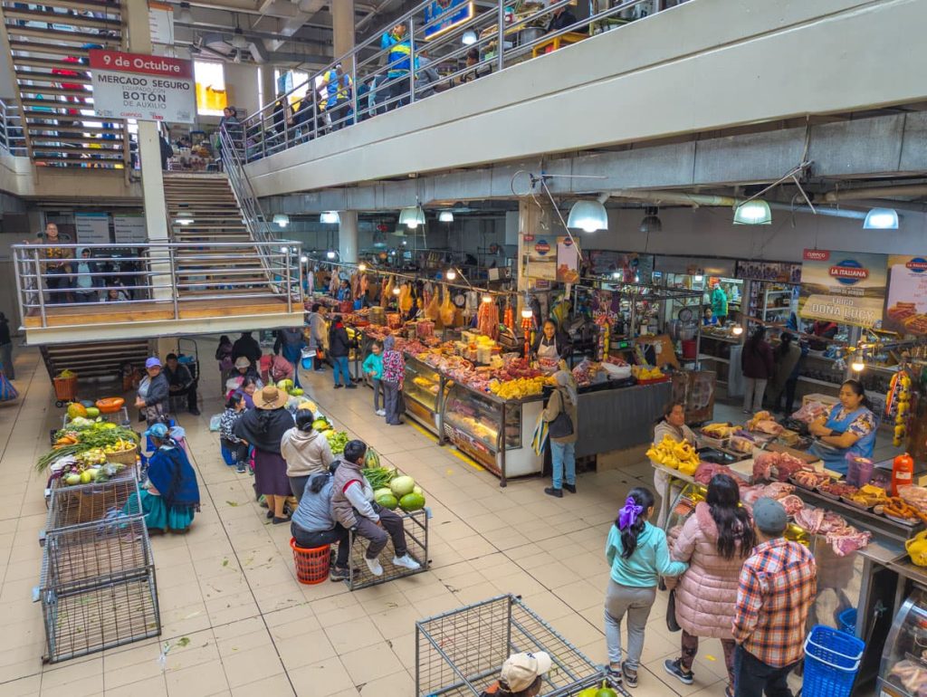 Shoppers and vendors interact on the lower level of Mercado 9 de Octubre in Cuenca, surrounded by meat counters and a few fresh produce stands.