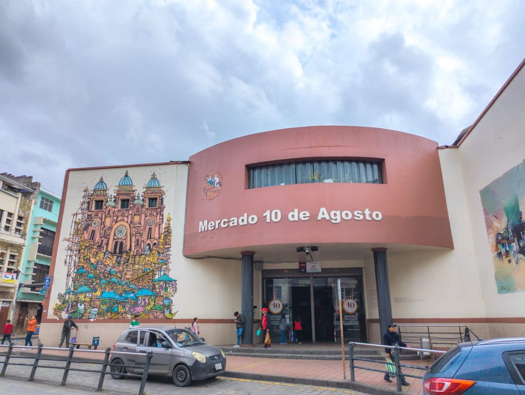 Exterior view of Mercado 10 de Agosto in Cuenca Ecuador, with its rounded facade and mural of the Cathedral on the wall.
