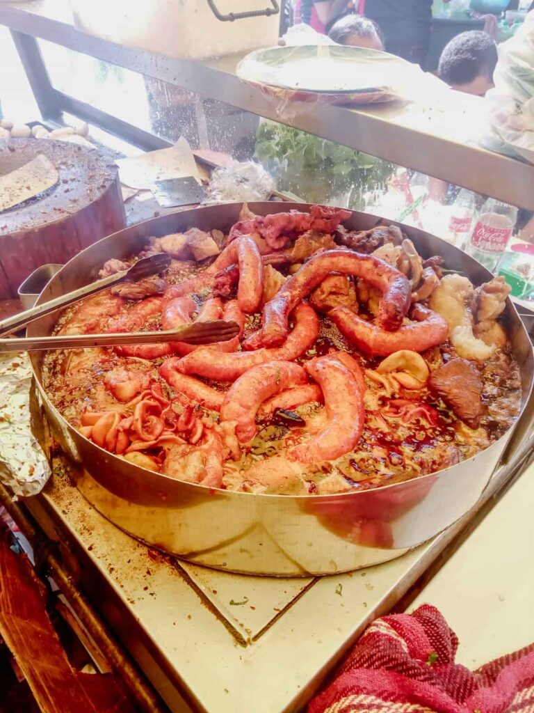 A Mexico City taco stand cooks sausage and other meats in a large pot. Next to the pot is a wooden cutting board and cleaver used to cut the meat for tacos.