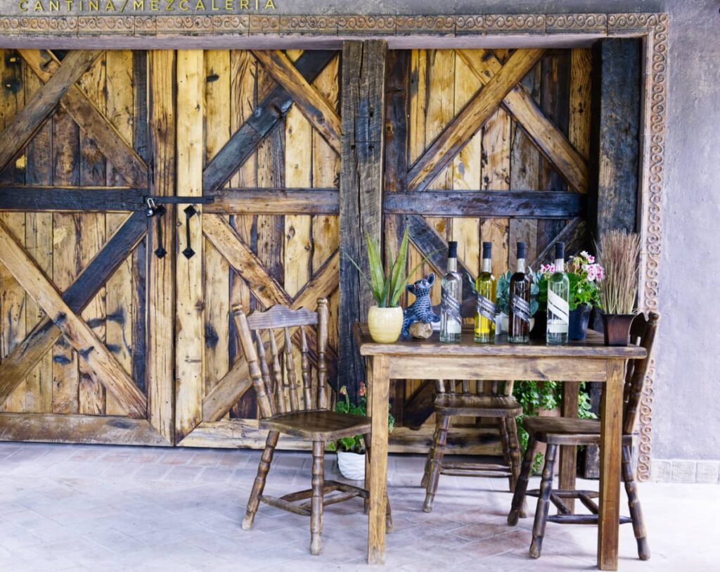 Several bottles of mezcal are lined up on a table for a mezcal tasting at Finca La Devocion near San Miguel de Allende. Behind is a large sliding barn door made of wood.