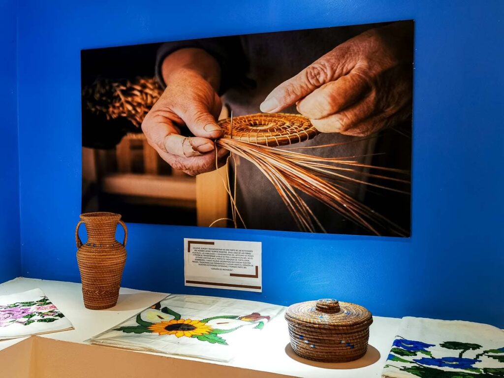 Bright blue wall with a photograph of a man's hands creating the bottom of a basket in copper.