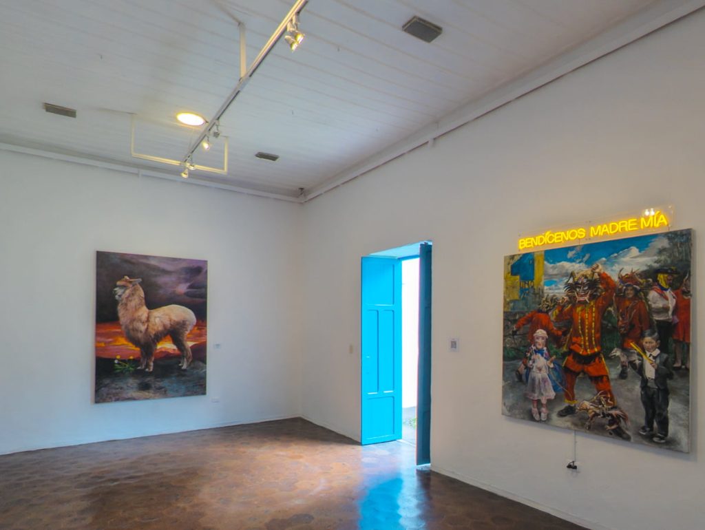 Modern gallery room in the modern art museum in Cuenca Ecuador featuring modern Ecuadorian artwork including a painting of a llama and neon-lit words that say “Bendícenos Madre Mía.”