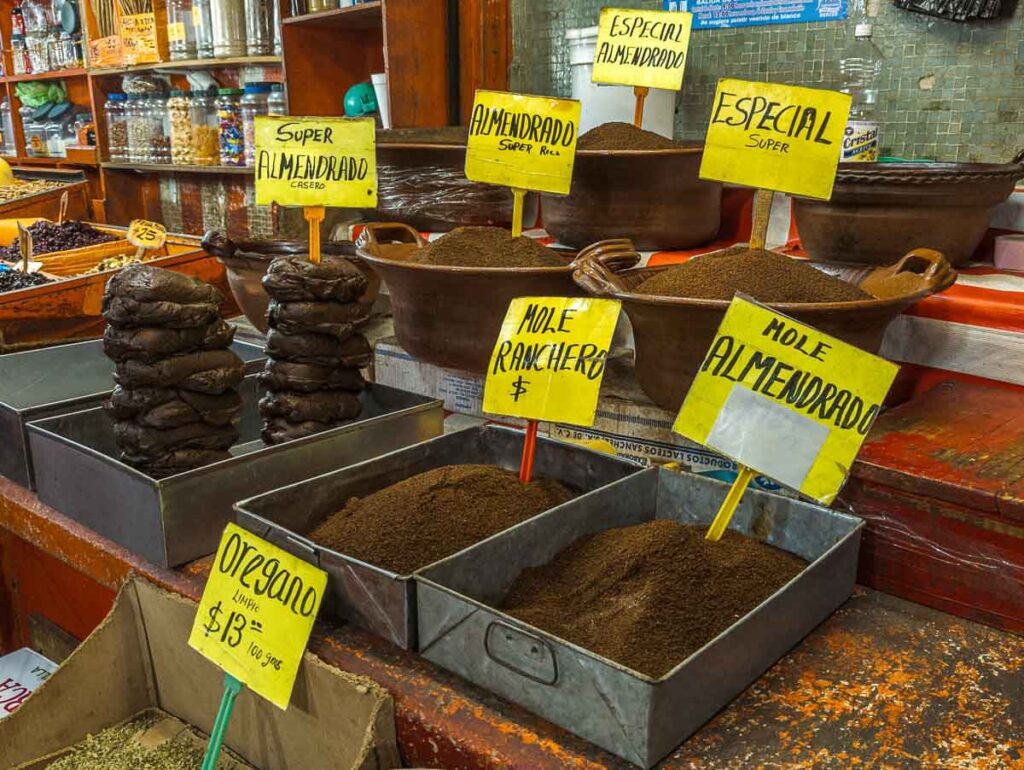 Mole paste and ground mole for sale at a Mexico City market stall. Bright yellow signs mark the type of mole but omit the price.