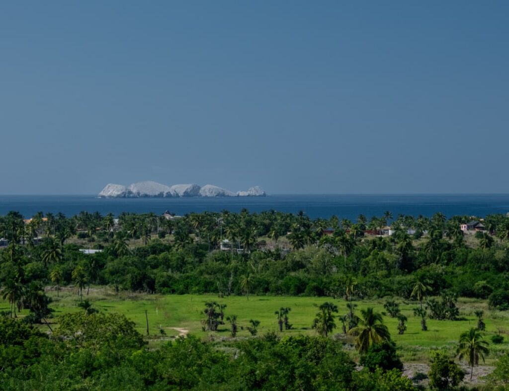 Panoramic view of Los Morros de Potosi, the iconic diving spot near Zihuatanejo, seen from a lush tropical landscape under a clear blue sky.