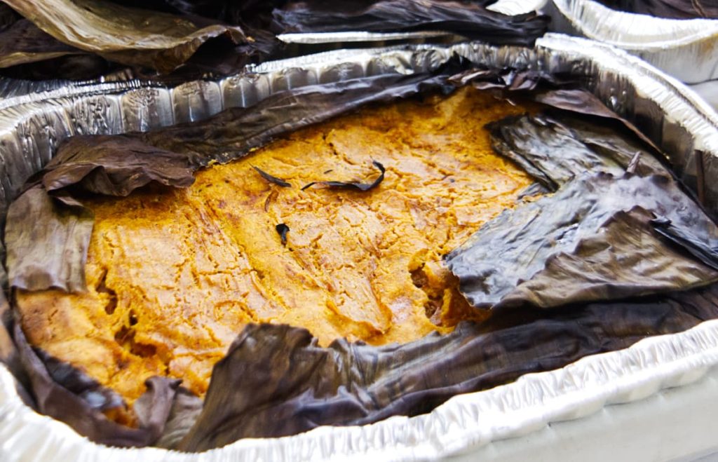 A traditional Day of the Dead food in the Yucatan, mukbilpollo aka pib is wrapped in banana leaves inside of a large aluminum tray. The banana leaves are open on the top to reveal the soft masa inside. Essentially a very large tamale.