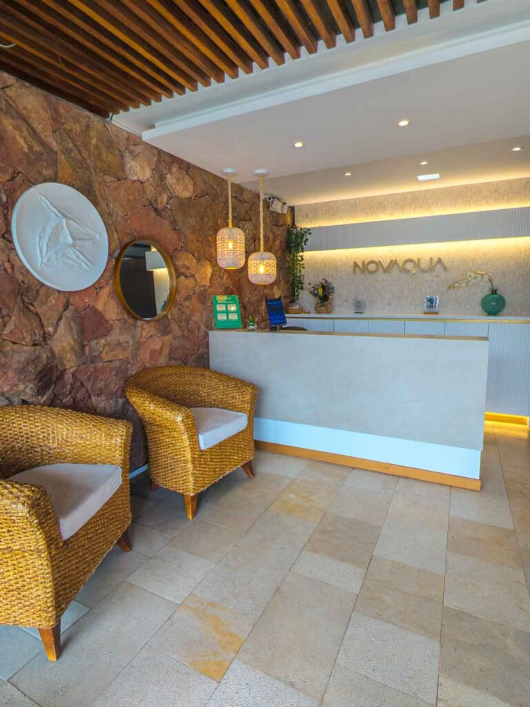 Welcoming reception area at Novaqua in Baños de Cuenca, with wicker armchairs, stone walls, and soft pendant lighting behind the check-in counter.