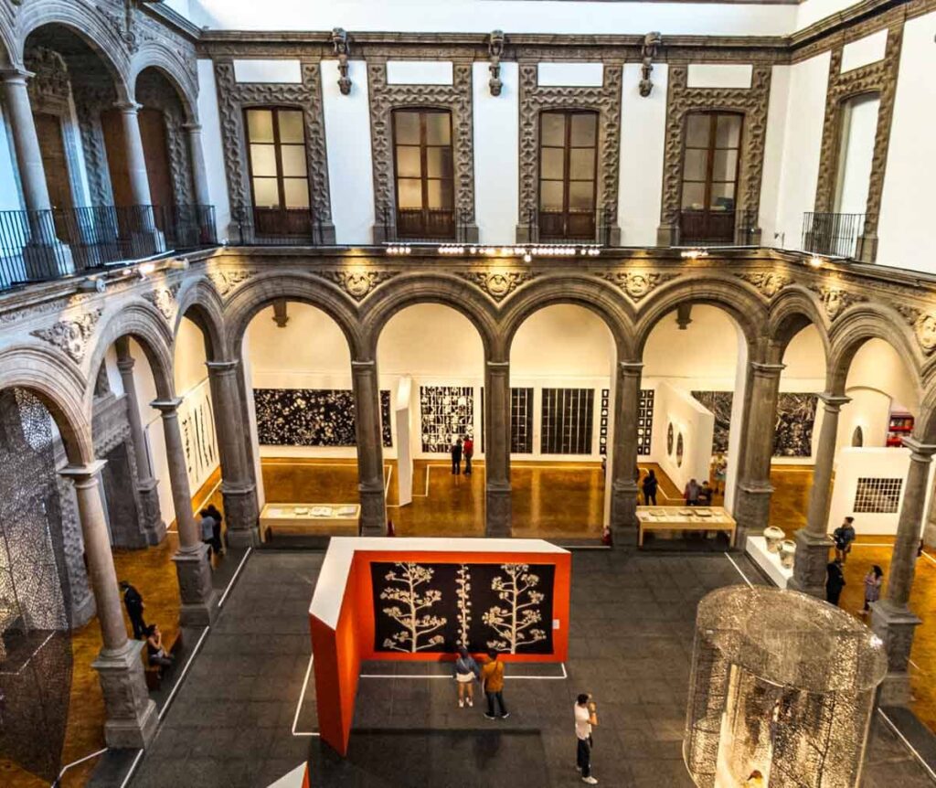 Multiple paintings and artworks with a few visitors in the Palacio de Cultura Museum in Mexico City.