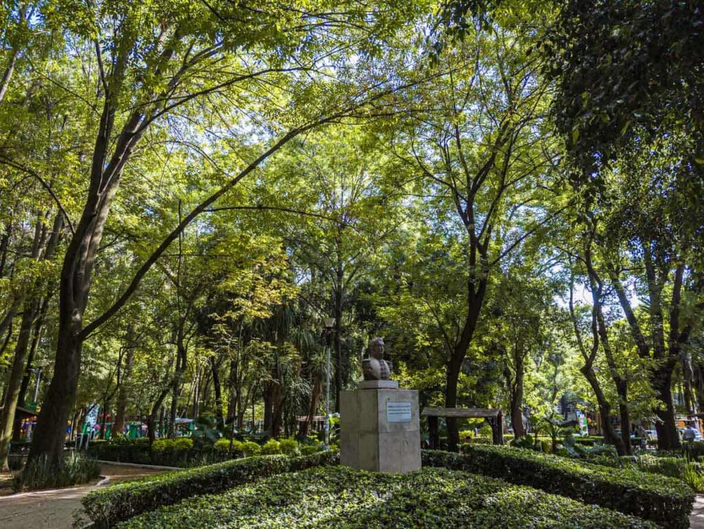 A bust statue surrounded by greenery and trees in Parque Mexico, La Condesa CDMX.