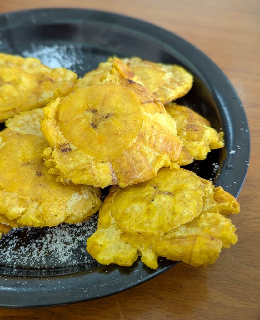 Plate of crispy patacones, a popular street food in Ecuador, sprinkled with salt and served on a black plate.