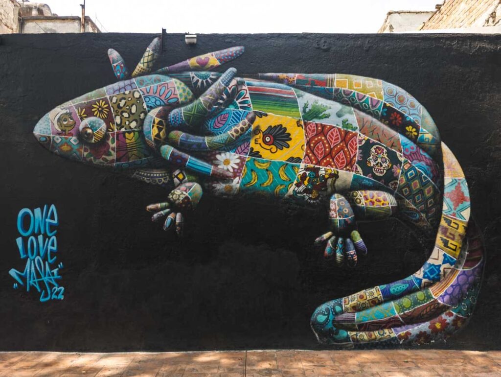 A large axolotl amphibian is painted with a patchwork design on a black background in this street mural in Mexico City.