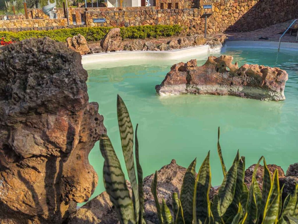 Close-up of the turquoise thermal waters at Piedra de Agua in Cuenca Ecuador, framed by volcanic rock and tropical plants near the pool’s edge.