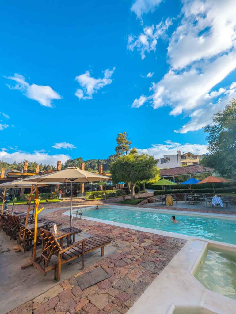 Thermal pool at Piedra de Agua Cuenca, surrounded by lounge chairs and umbrellas, with bright blue skies and peaceful garden surroundings.