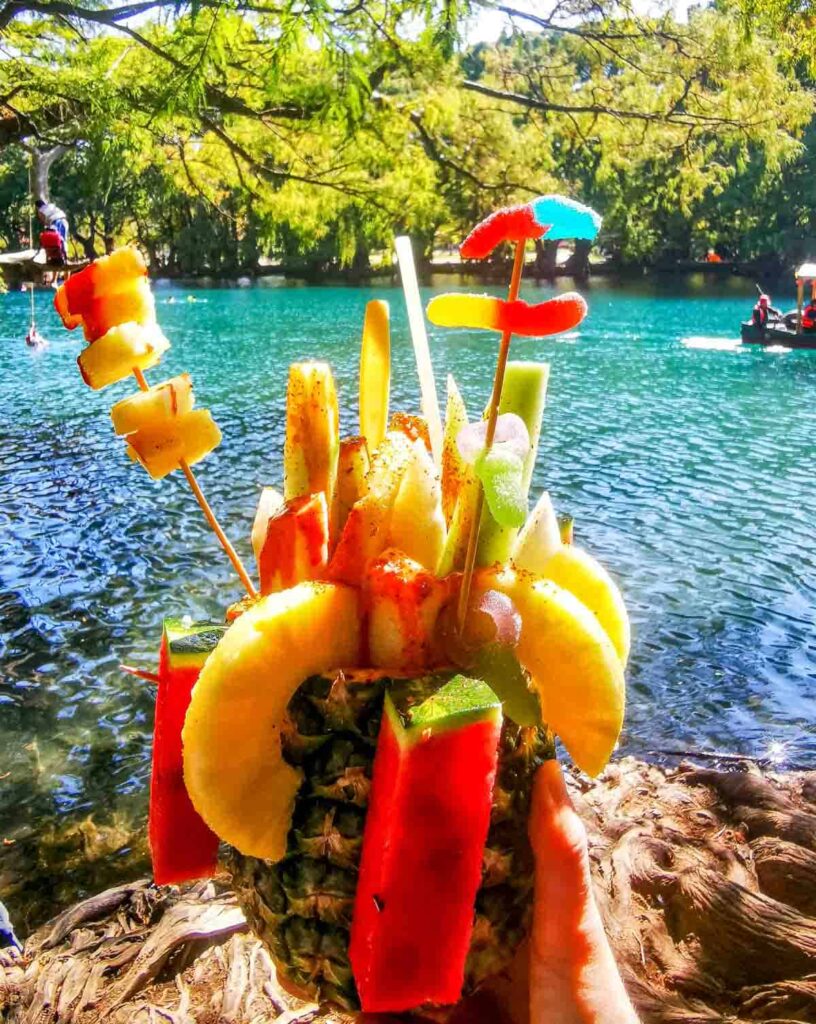 Different fruits sticking out of a pineapple, also known as pina loca with the lake in the background at Camecuaro, Michoacan.