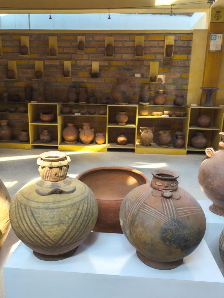 Pre-Columbian ceramic pottery with anthropomorphic features displayed inside a Cuenca museum, arranged neatly against a rustic brick wall.