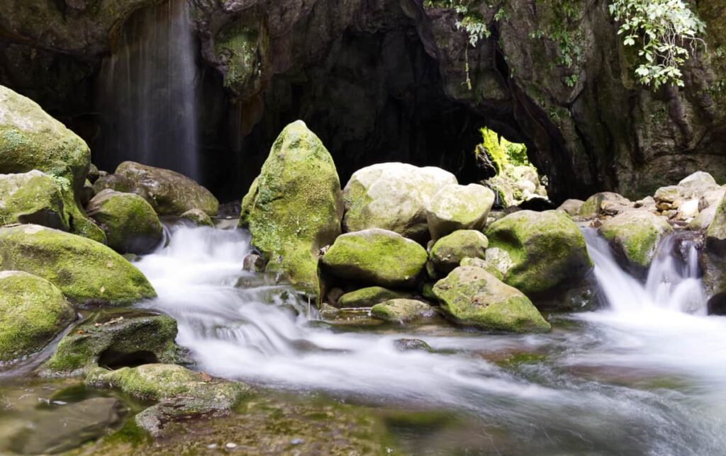 In this long exposure photograph, water flows down the rocks in small waterfalls. In the background is the larger waterfall of Puente de Dios.