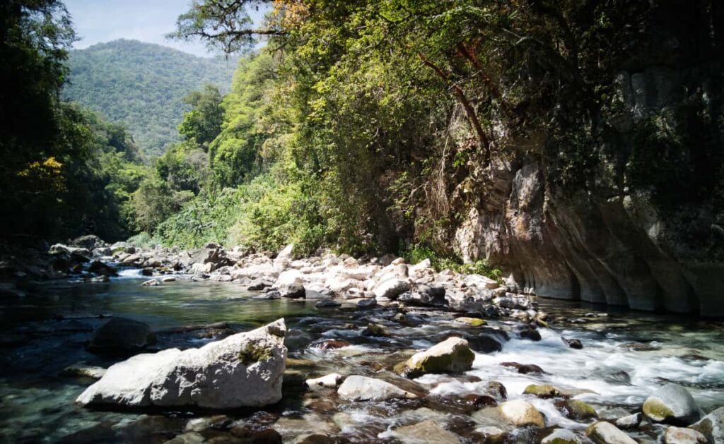 A picturesque scene of the river at Puente de Dios. Lots of Rocks in the foreground and mountains in the background.