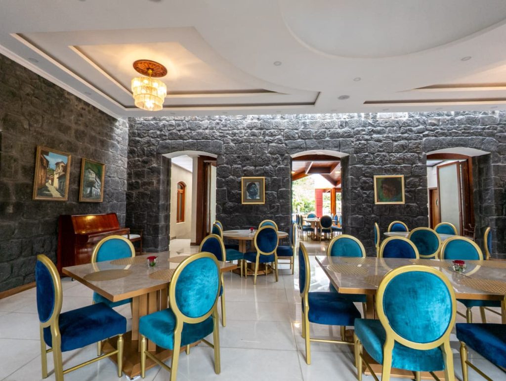 Elegant dining room at Sangay Hotel in Baños, Ecuador features blue velvet chairs, stone walls, and chandeliers, offering a refined experience.