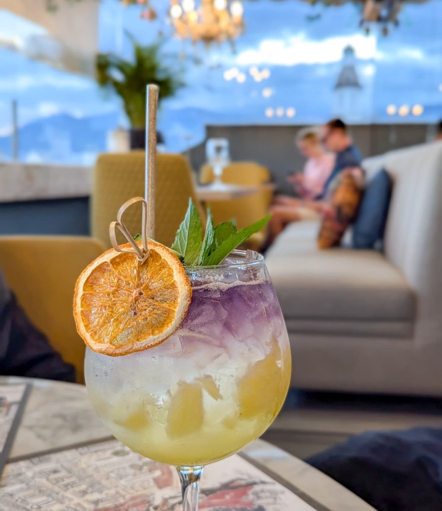 A vibrant layered cocktail garnished with dried orange and mint sits on a table at a stylish rooftop bar in Cuenca Ecuador. Enjoying creative drinks with a view is a great option if you're looking for what to do in Cuenca at night.