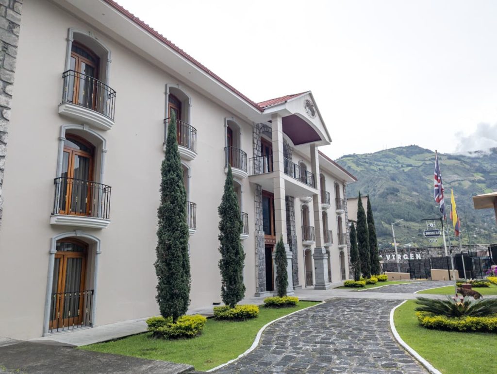 Impressive colonial-style hotel with arched windows, manicured lawns, and mountain views in the background. This upscale hotel stands out among the best places to stay in Baños, Ecuador.