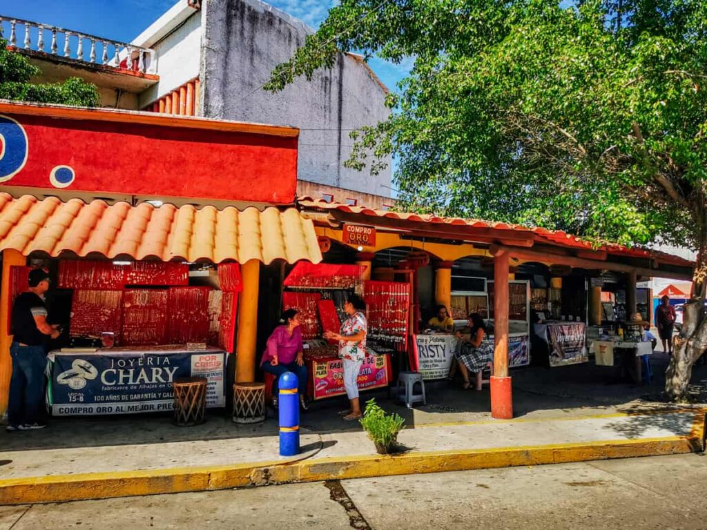 Bright orange facade of the booths at the silver market in Petatlan, a thing to do near Zihuatanejo. People engage in conversation under the shade.