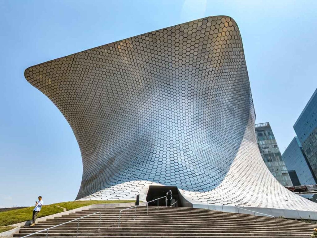 The exterior view of Soumaya Museum in Mexico City features a silver metal structure in an oblong shape.