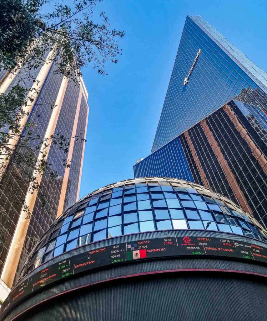The circular glass Stock Market Museum surrounded by tall buildings under a clear blue sky in Mexico City.